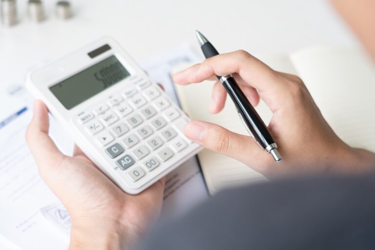 A hand holding a white calculator with a black pen, reviewing financial documents, demonstrating calculator benefits for accident compensation evaluation.