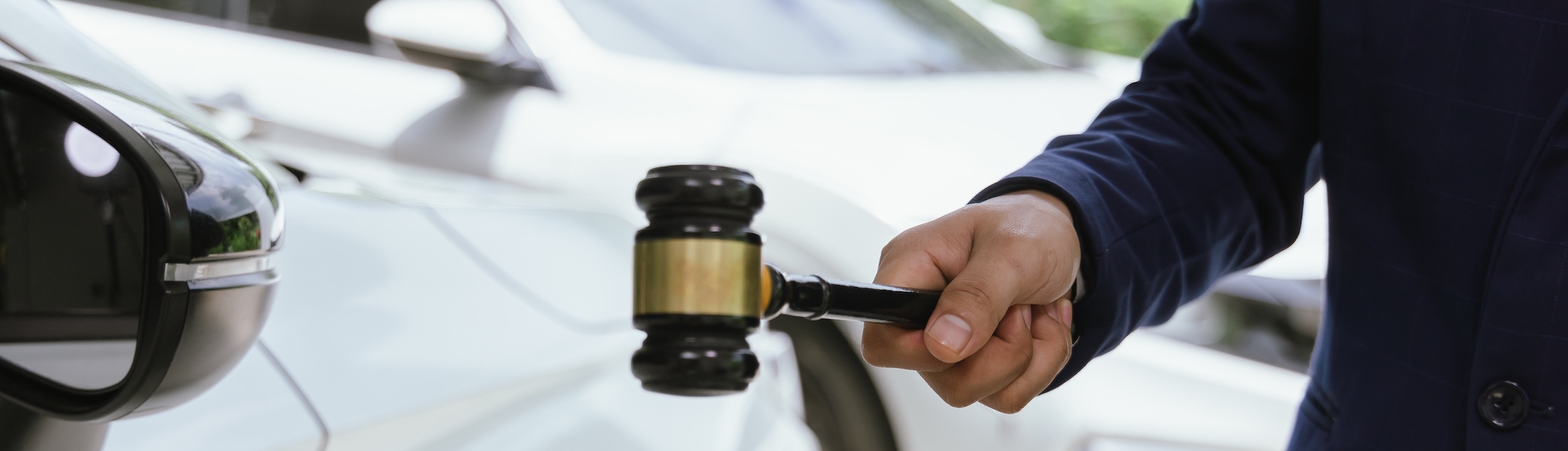 A hand in a dark sleeve holding a wooden judge's gavel with black and white cars blurred in the background representing injury claim value estimation legal process.