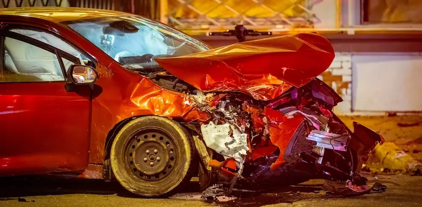 A motor vehicle crash with severe front-end damage to a red sedan after a nighttime collision.
