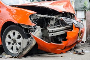 A severely damaged orange car with a crushed front end which is showing extensive collision damage from two car accidents in Tennessee.