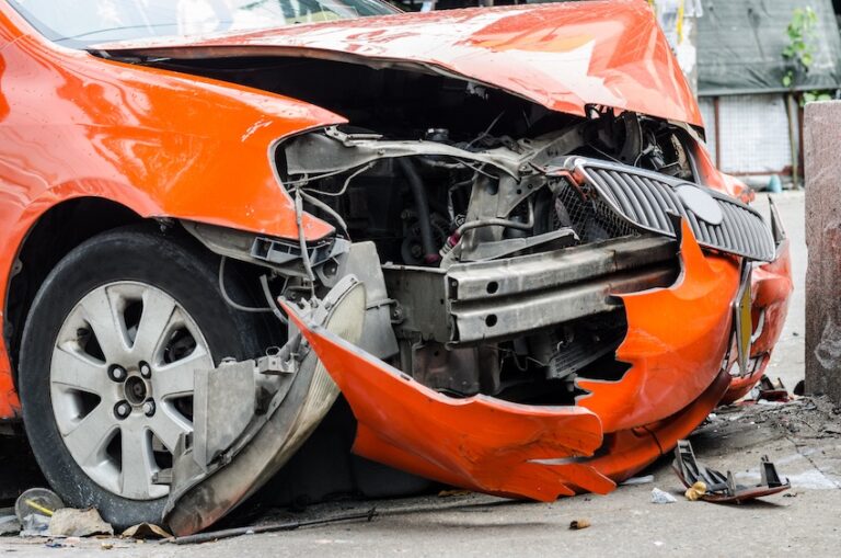 A severely damaged orange car with a crushed front end which is showing extensive collision damage from two car accidents in Tennessee.