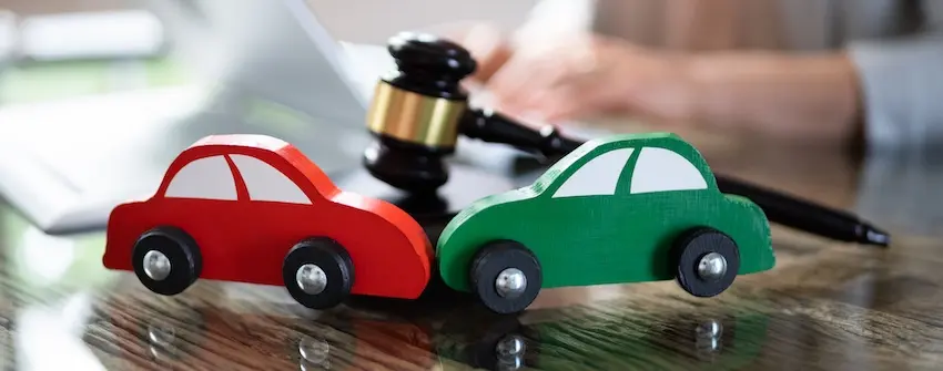 Red and green toy cars with a legal gavel representing car accident litigation and insurance claim settlement at Mogy Law Firm in Tennessee.