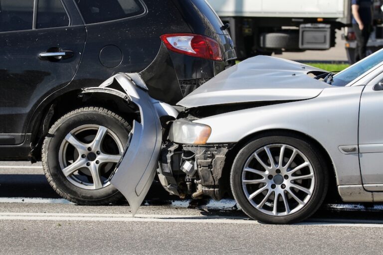 The crumpled front end of a silver sedan is pressed into the rear bumper of a black SUV on a busy roadway in Tennessee with a truck visible in the background depicting one of the most common car accident types the rear-end collision and the extensive vehicle damage it causes and could use help from Mogy Law Firm.