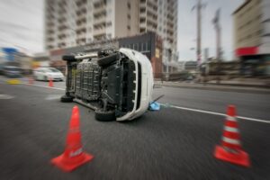 A white vehicle lies on its side in the middle of a city street surrounded by orange traffic cones depicting the dangerous aftermath of a rollover accident that would require victims to seek immediate legal representation from a rollover accident attorney at Mogy Law Firm in Tennessee.