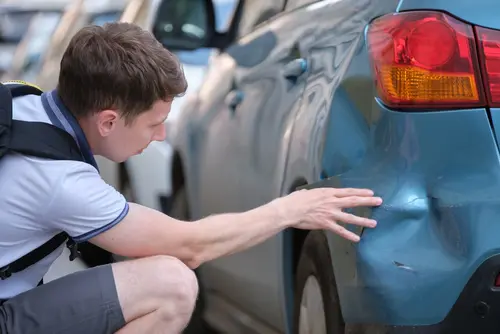 A man looking at a dent on his blue car after a hit-and-run accident.